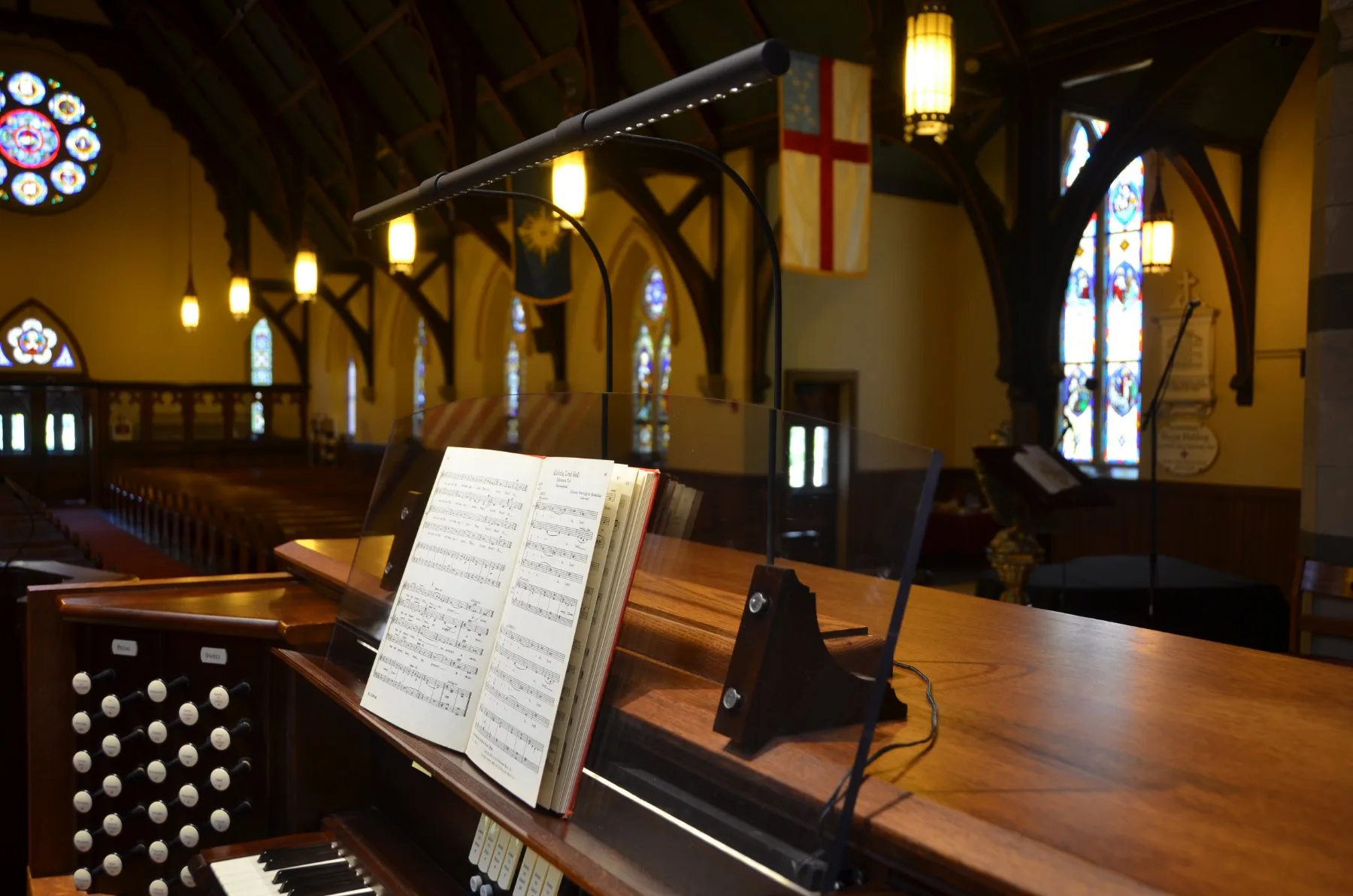 Brass Ektralamp organ music lamp lighting the sheet music on an organ console in a stained-glass church